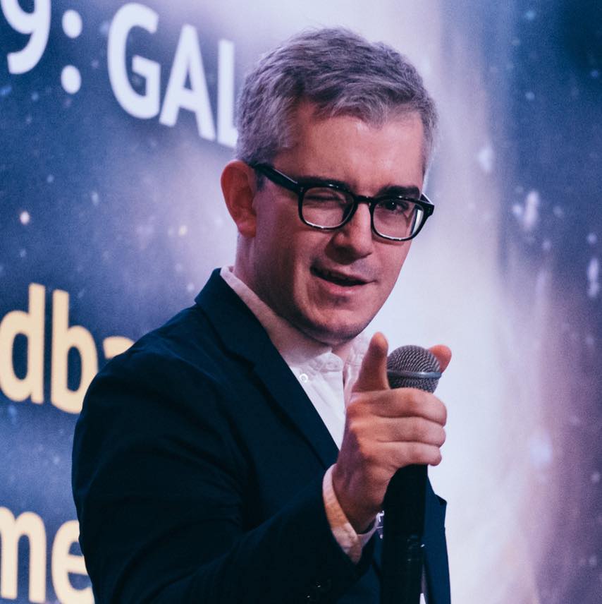 Travis Fischer speaking into a microphone during an astronomy talk.